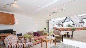 Un salon moderne avec un canapé, des fauteuils et une table basse. On y trouve un téléviseur posé sur un meuble, une cheminée et une vue sur l’extérieur grâce à de grandes fenêtres.