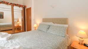 Une chambre à coucher avec un lit, deux lampes de chevet, une table de chevet en bois, un miroir et une porte.