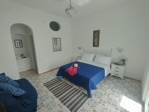 Ein Schlafzimmer mit einem Bett, einem Nachttisch, einer Kommode, einem Spiegel und einer Tür zu einem anderen Raum.