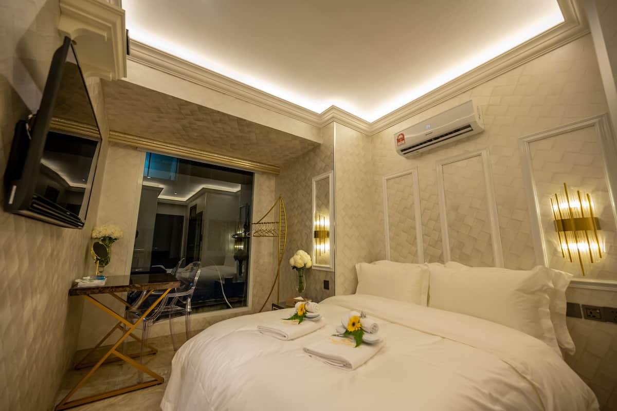 A hotel room with a large bed, a desk with a chair, a mirror, and a wall-mounted air conditioner.