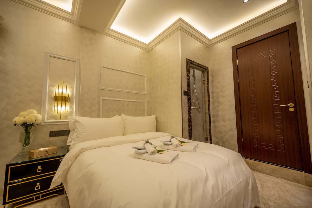 A hotel room with a large bed, a nightstand, a mirror, a wooden door, and a wall-mounted light fixture.