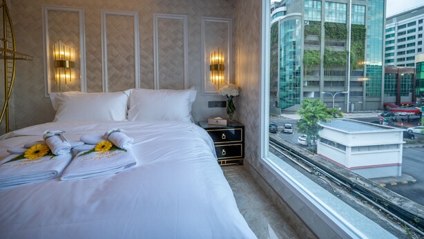 A hotel room with a neatly made bed, a nightstand with a lamp, and a view of the city through the window. - A Residence - A Member of The Luxury Stay Group (Kota Kinabalu)