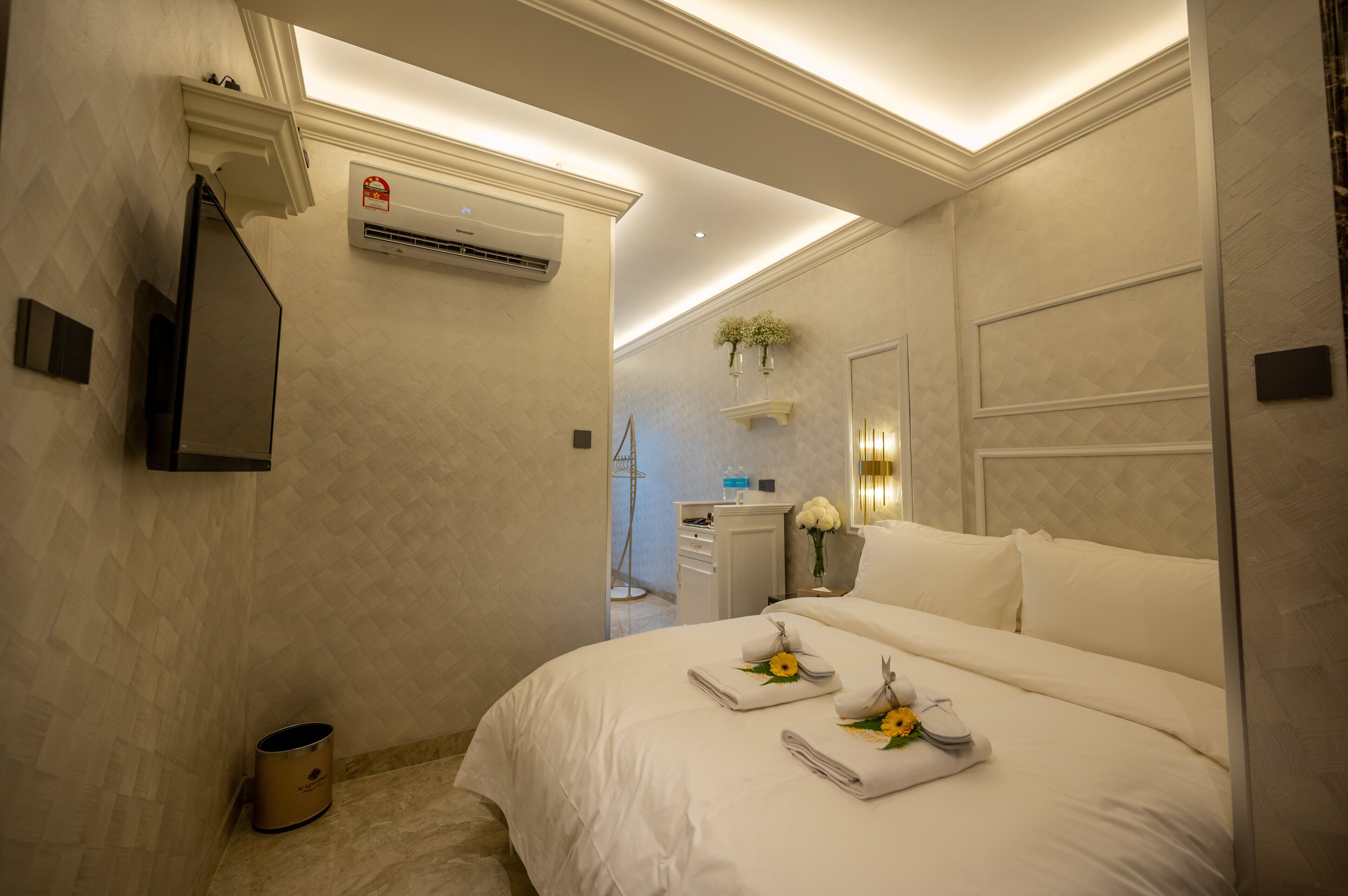Una habitación de hotel con cama, mesita de noche, aire acondicionado, espejo y un pequeño cubo de basura.