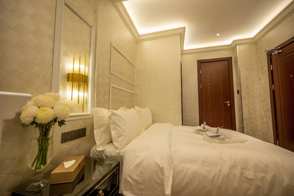 A hotel room with a bed, a vase of flowers, a bedside table, and a mirror.