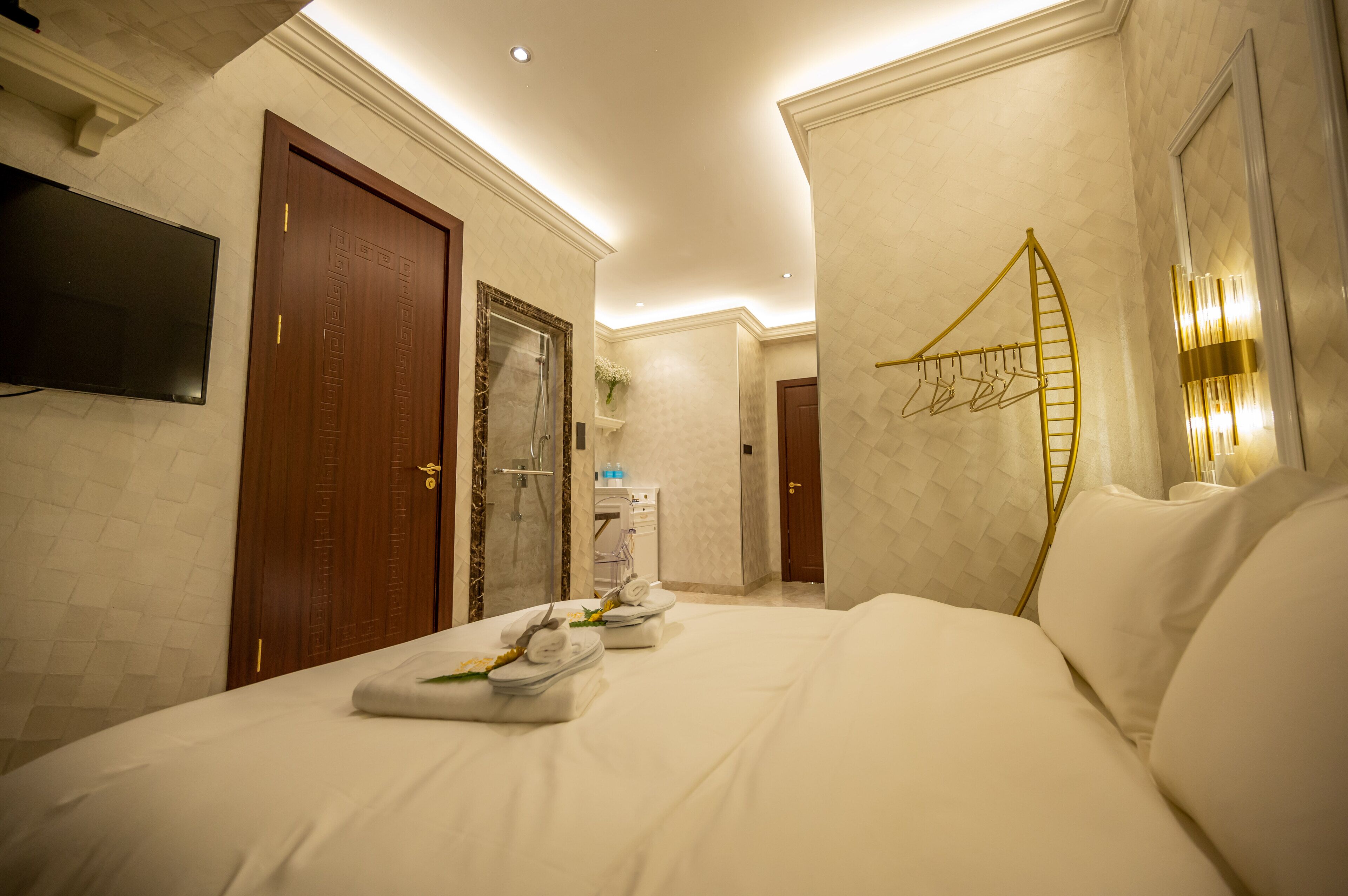 A hotel room with a large bed, a TV mounted on the wall, a shower area, and a wall-mounted towel rack.