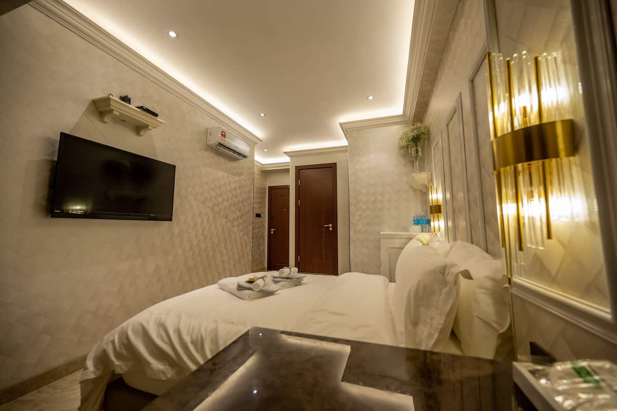 A hotel room with a bed, a flat-screen TV mounted on the wall, a bedside table, and a mirror with a light fixture.