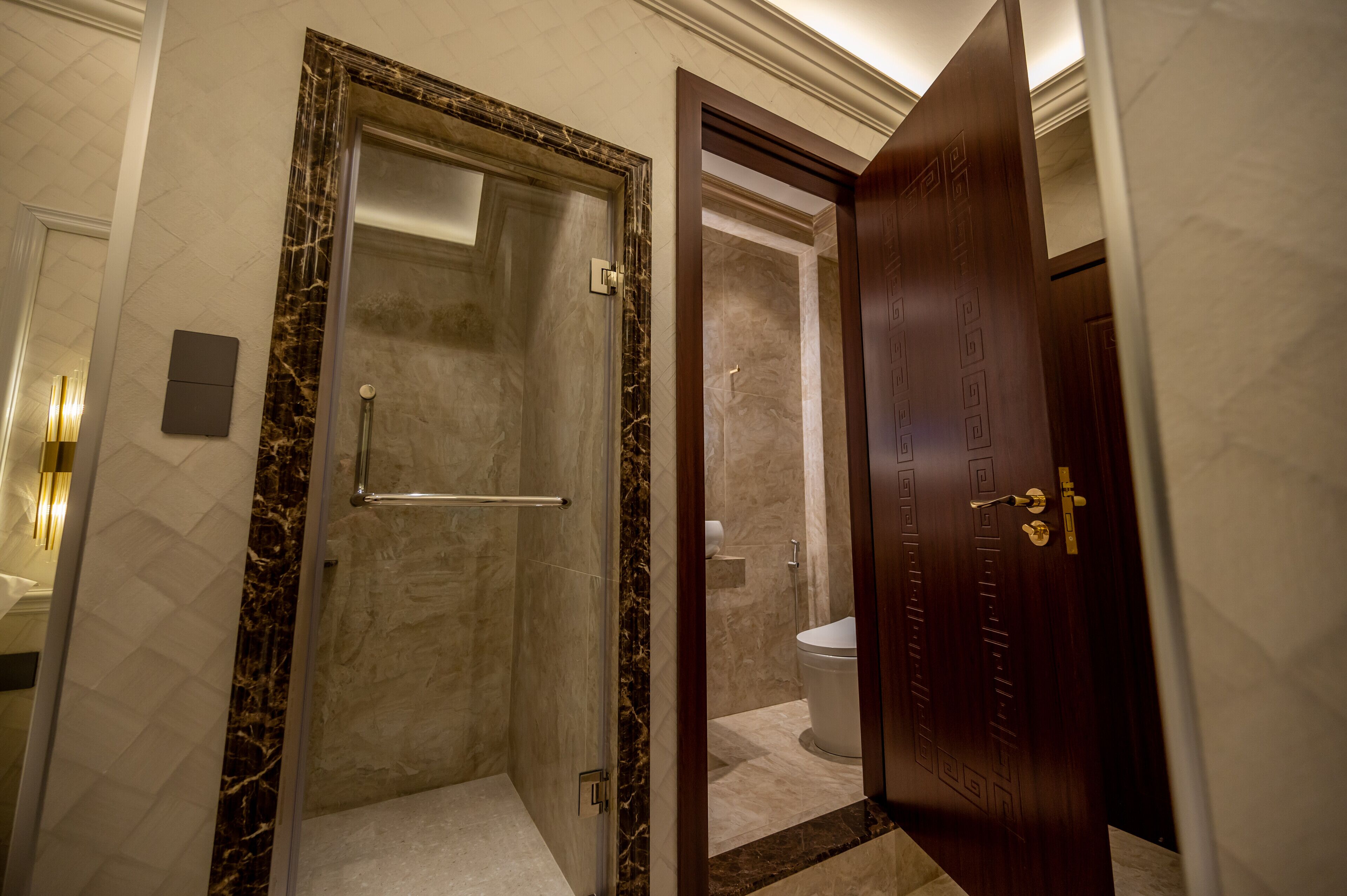 A modern bathroom with a glass-enclosed shower, a toilet, and a wooden door with a keypad lock.