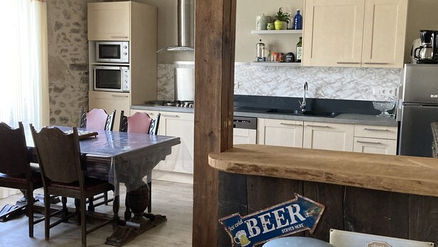 A kitchen with wooden beams, a dining table with chairs, and a bar area with stools. - Large, bright apartment (Argentat-sur-Dordogne)