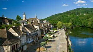 A riverside town with historic buildings, a church, and a view of a forested hill. - Large, bright apartment (Argentat-sur-Dordogne)