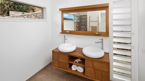 Un baño con dos lavamanos blancos, un mueble de tocador de madera, un espejo grande y una ventana con vistas a zonas verdes.