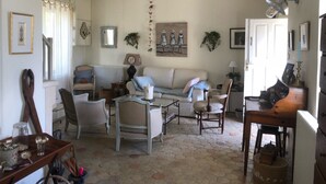 Un saló d'estar acollidor amb un sofà, cadires, una taula de centre i una taula de menjador. Hi ha objectes decoratius a les parets i una finestra amb cortines.