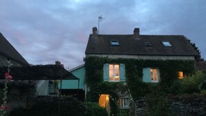 Una casa amb teulada inclinada, dues finestres visibles amb persianes i una xemeneia.