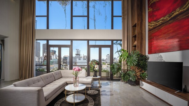 A modern living room with a large sofa, a coffee table, and a TV. There are large windows with a city view. - Tashi Oasis Hotel & Apartment (Da Nang)
