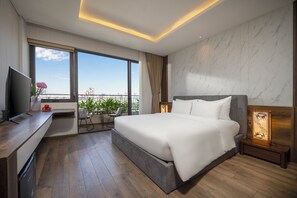 A modern hotel room with a large bed, a TV, a desk, and a balcony with plants. - Tashi Oasis Hotel & Apartment (Da Nang)
