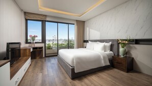 A modern hotel room with a large bed, a desk, and a view of the city. - Tashi Oasis Hotel & Apartment (Da Nang)