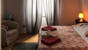 Una habitación de hotel con una cama, una silla, una lámpara y una ventana con cortinas.