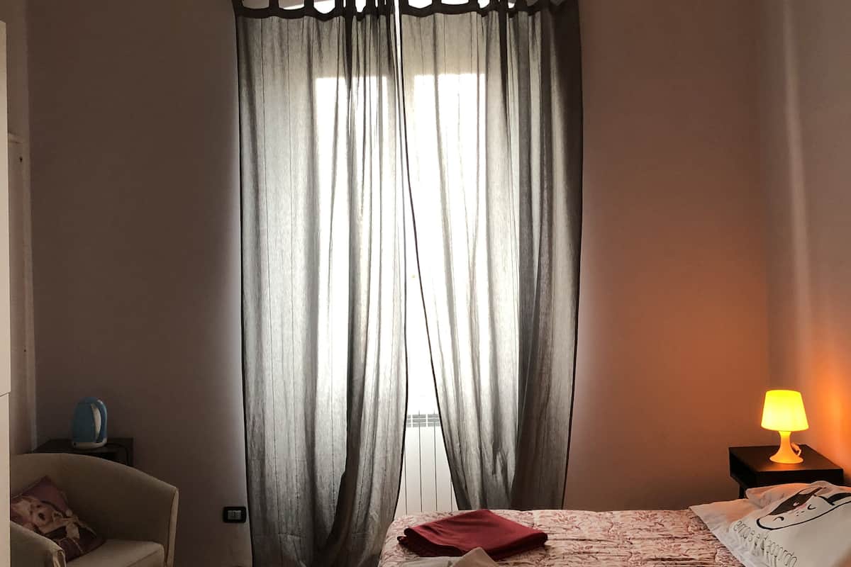 A hotel room with a bed, a chair, a lamp, and a window with curtains.