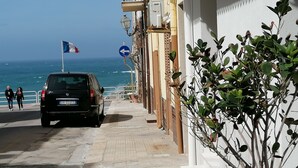 Una calle estrecha con un coche negro estacionado al lado, una acera para peatones y vistas al mar.