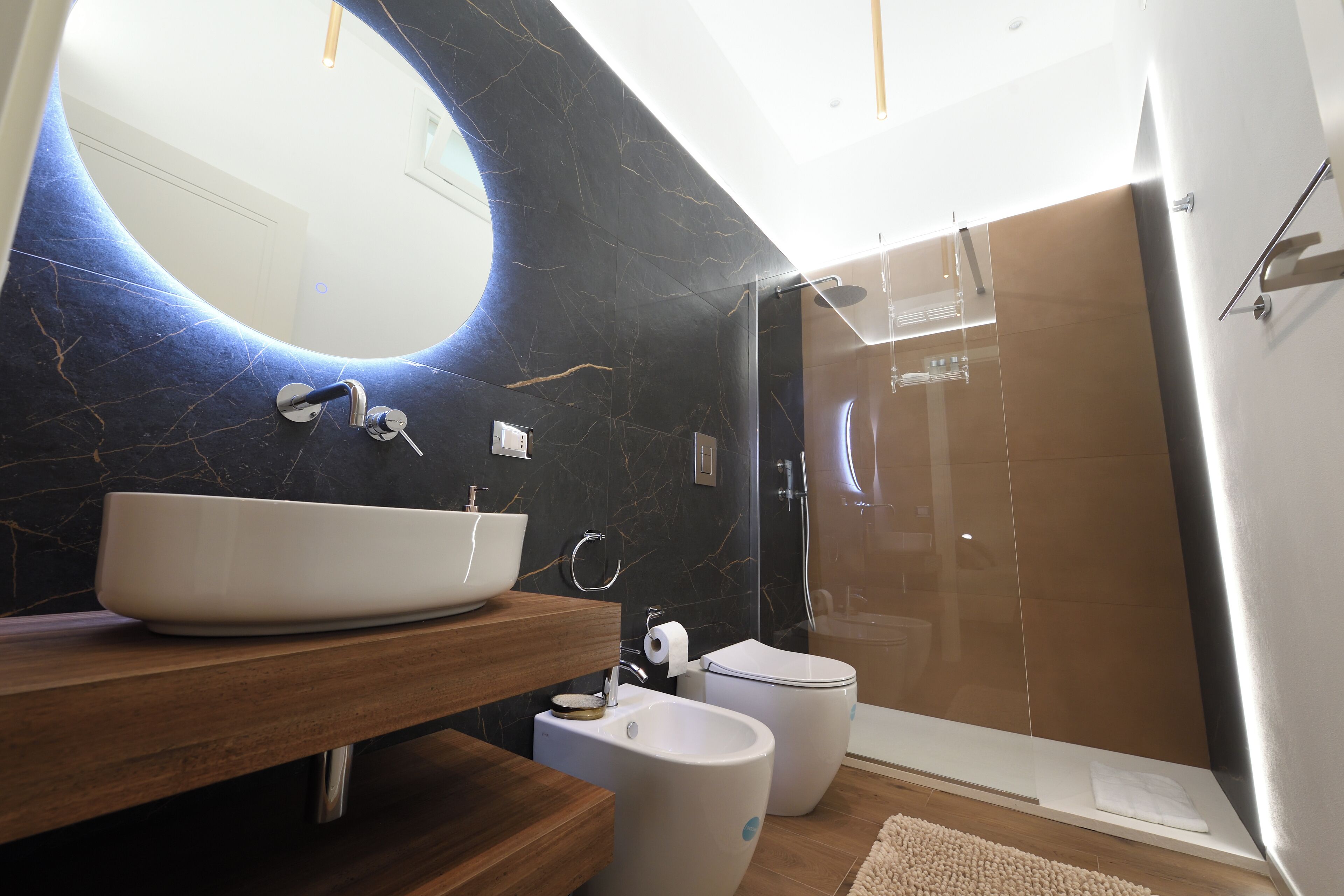 Een moderne badkamer met een grote, ovale spiegel, een witte wastafel, een toilet en een douchecabine met glazen wanden.