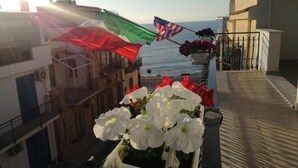 Un balcón con vista al mar, una bandera y flores en macetas.