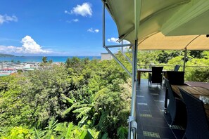 A terrace with a table and chairs, overlooking a lush green landscape and a distant view of the sea and buildings. - Andaman Hills by Lofty (Patong)