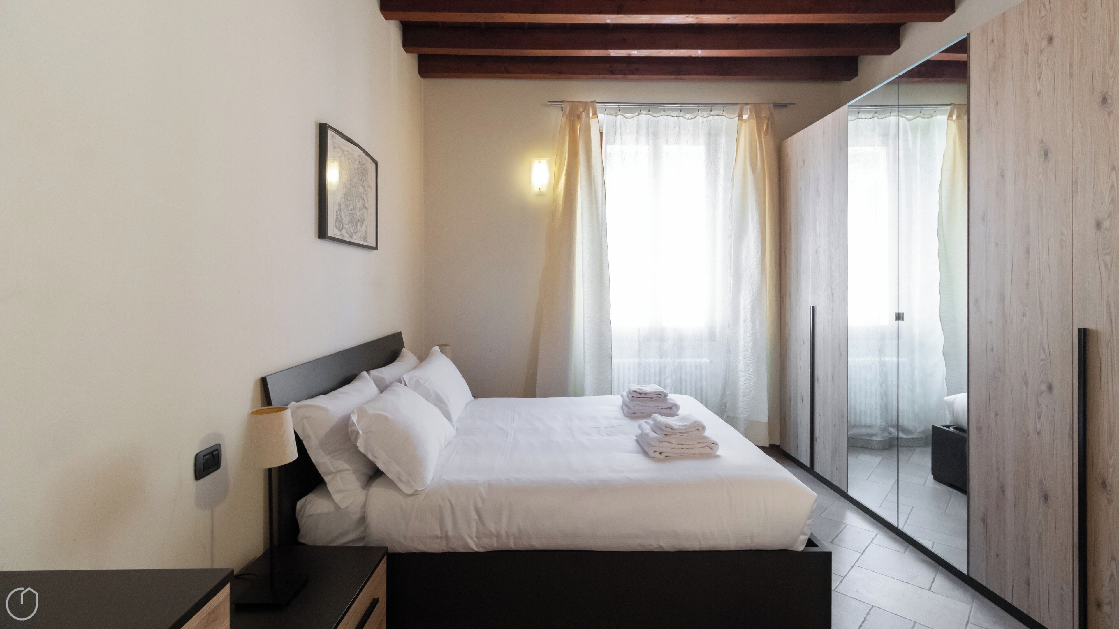 Une chambre à coucher comprenant un lit, une table de chevet, une lampe, un tableau encadré et une porte coulissante donnant sur un balcon.