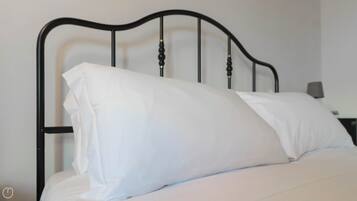 A bed with a white mattress and pillows, a black metal headboard, and a bedside table with a lamp.