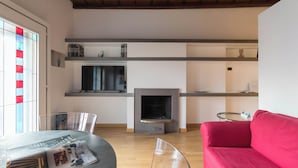 Un salon moderne avec une cheminée, un canapé rouge, une table basse en verre et un téléviseur fixé au mur.