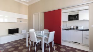 A compact kitchen with a dining area, white cabinets, a red partition, and a tiled floor.