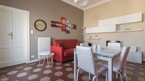 A modern living room with a red sofa, white chairs, a glass dining table, and a white cabinet.