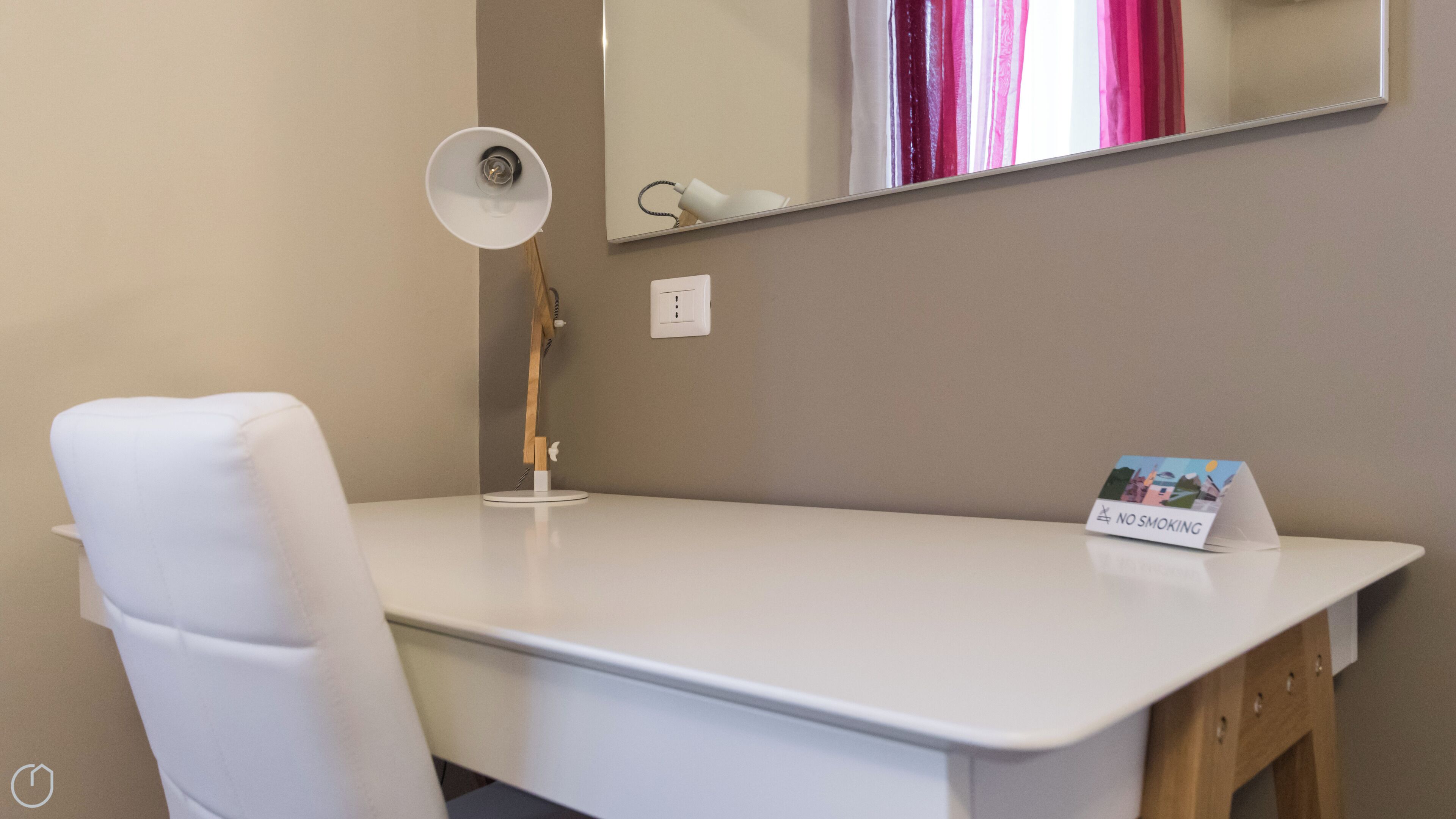 Een wit bureau met een lamp, een stoel, een spiegel en een bordje 'Niet roken'.