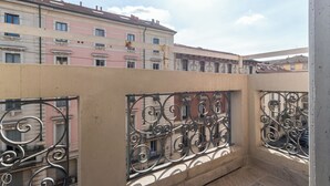Een balkon met gedetailleerd metalen hekwerk, een beige muur, en uitzicht op meerverdiepingen met roze en beige gevels.