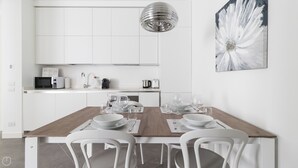 Een moderne keuken met witte kasten, een houten eettafel met witte stoelen, en een groot abstract schilderij aan de muur.