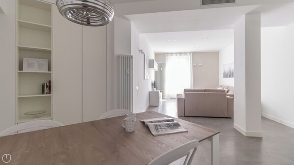 A modern, well-lit living area with a wooden dining table, a sofa, and a kitchen in the background. - Italianway Comfort - Vincenzo Monti 29 B (Milan)