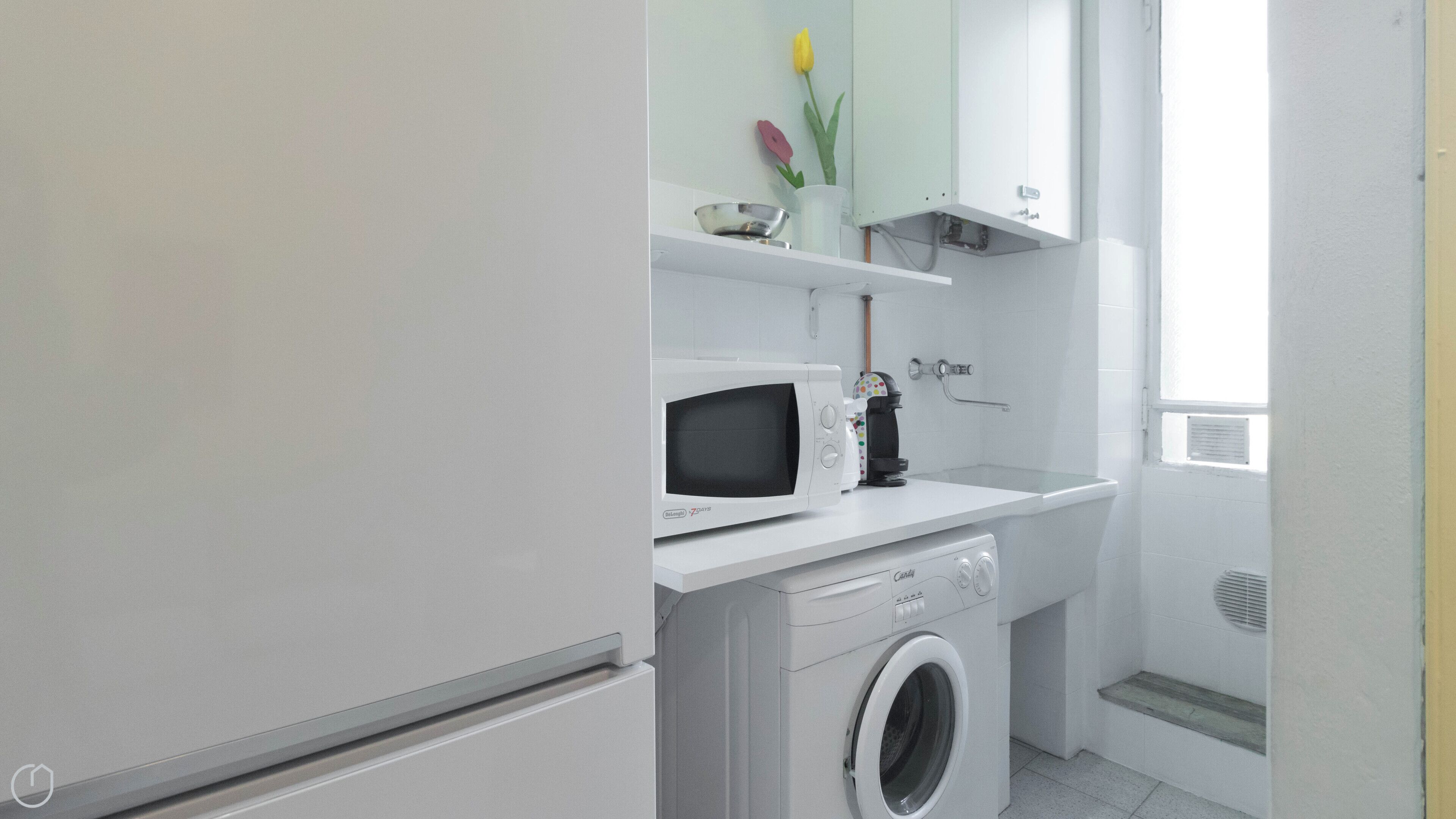 A compact laundry room with a washing machine, a microwave, and a small shelf with decorative items.