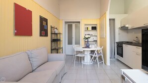 Ett kompakt bostadsutrymme med en soffa, ett matbord med stolar, ett köksområde med spis och kylskåp samt en dörr som leder till ett annat rum.