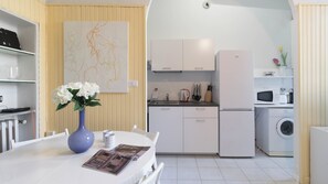 Uma cozinha moderna com armários brancos, máquina de lavar embutida e um espaço de jantar com mesa e cadeiras.