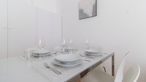 Une table à manger dressée avec de l’argenterie blanche, des verres à vin et des couverts, le tout dans un style minimaliste, et un tableau encadré accroché au mur.