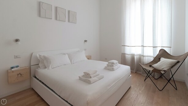 Une chambre à coucher au style minimaliste, avec un lit, une chaise et une table de chevet.