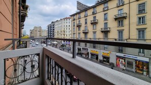Un balcon doté d’une balustrade en métal donnant sur une rue bordée de divers commerces et bâtiments.