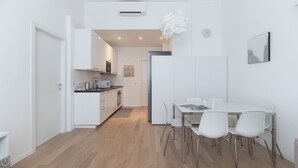 Une cuisine moderne avec des meubles blancs, un coin repas doté d’une table et de chaises blanches, et une horloge visible au mur.