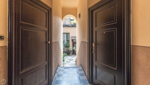 A corridor with two dark wooden doors leading to a courtyard with tiled flooring and potted plants. - Italianway - Jacopo dal Verme 4 (Milan)