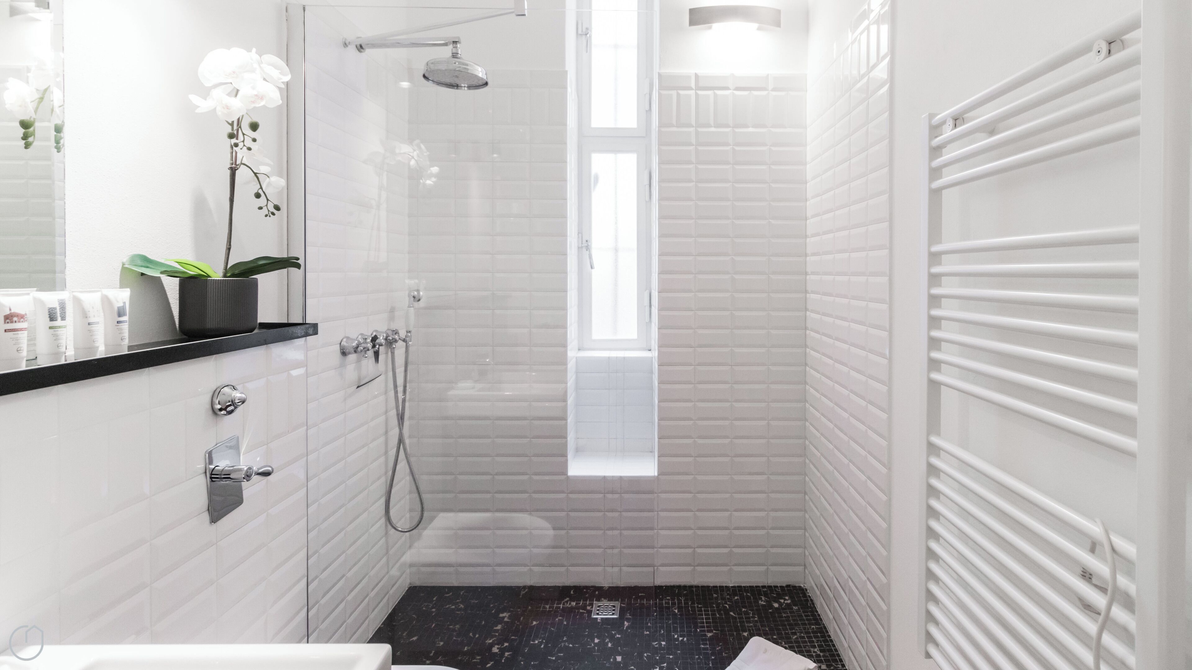 A modern bathroom with white subway tiles, a glass-enclosed shower, a black marble floor, and a small potted orchid on the vanity.