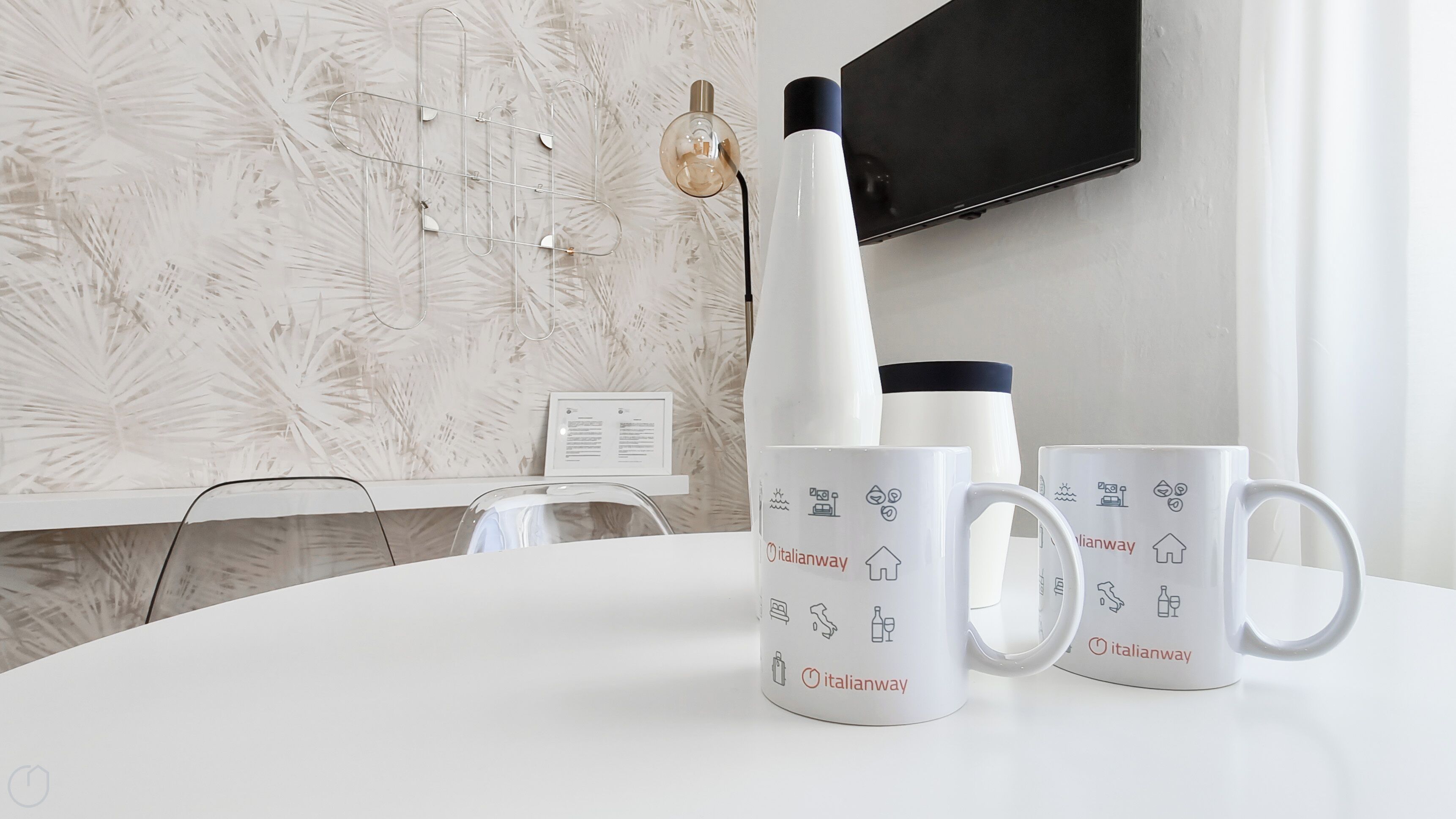 A white table with three Italianway mugs and a white water bottle.