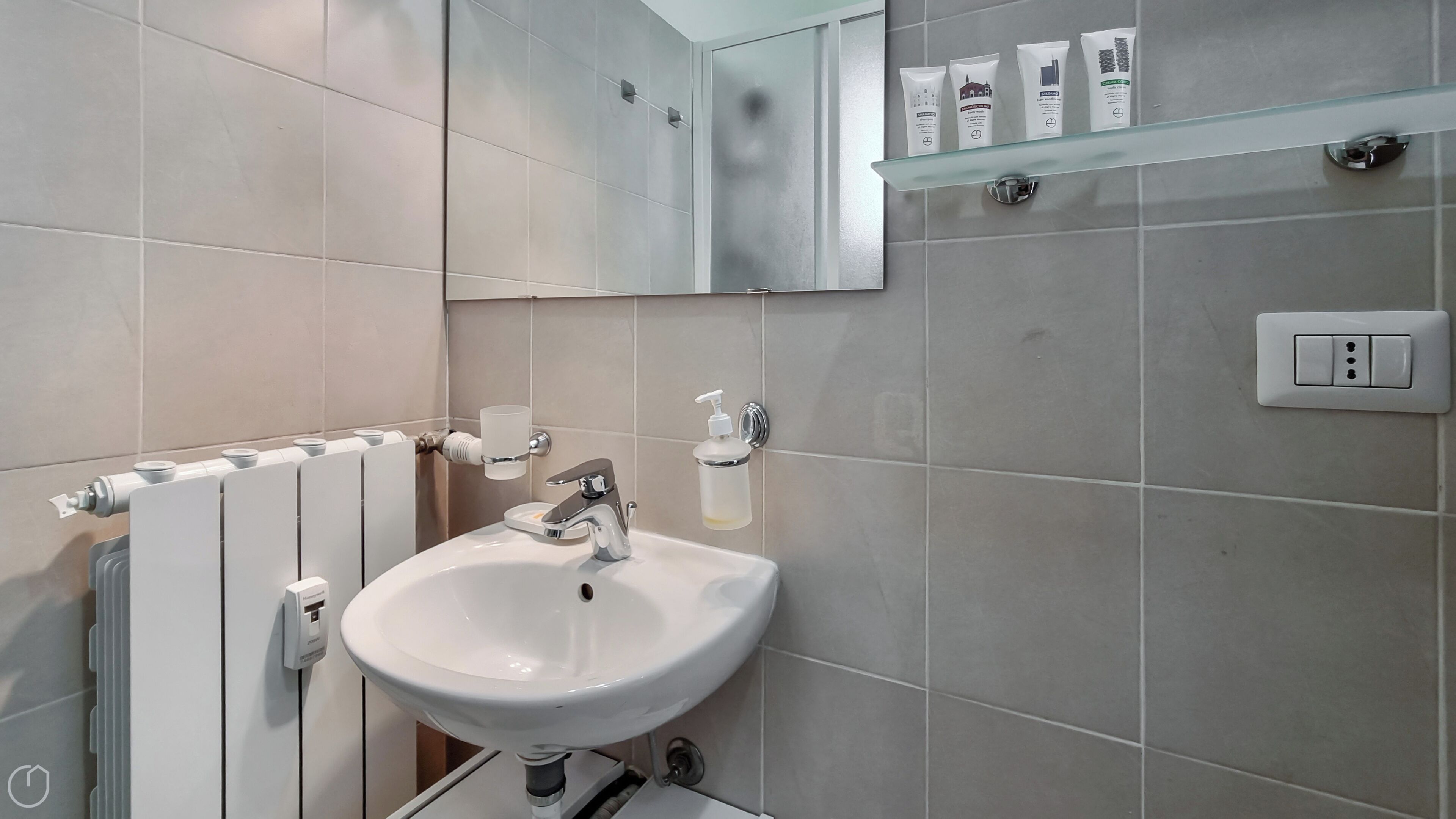 A bathroom with a white sink, a mirror, and a glass shelf with toiletries.