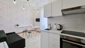 A modern kitchen with white cabinets, a stainless steel sink, and a built-in oven. There is a dining area with a table and chairs, and a small potted plant on the wall. - Italianway - Gallura 9 (Milan)