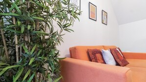 A room with a large green plant, an orange sofa, and two framed pictures on the wall. - Italianway Easy - Plinio 64 (Milan)