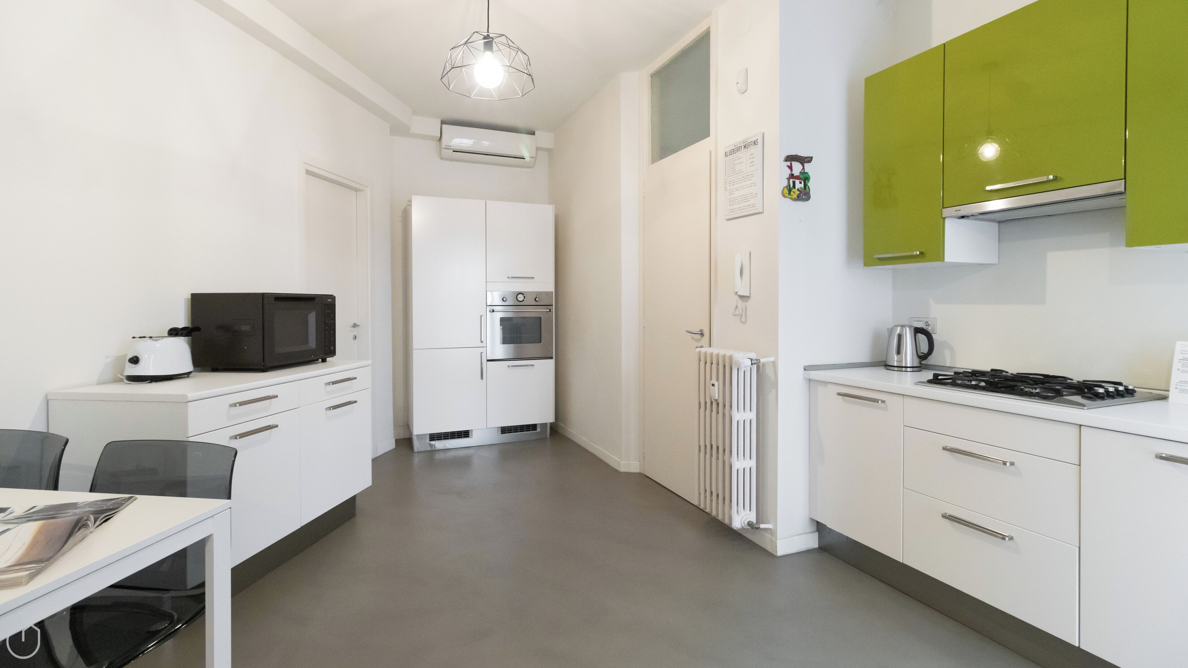 A modern kitchen with white cabinetry, a green accent wall, a microwave, an oven, a kettle, and a gas stove.