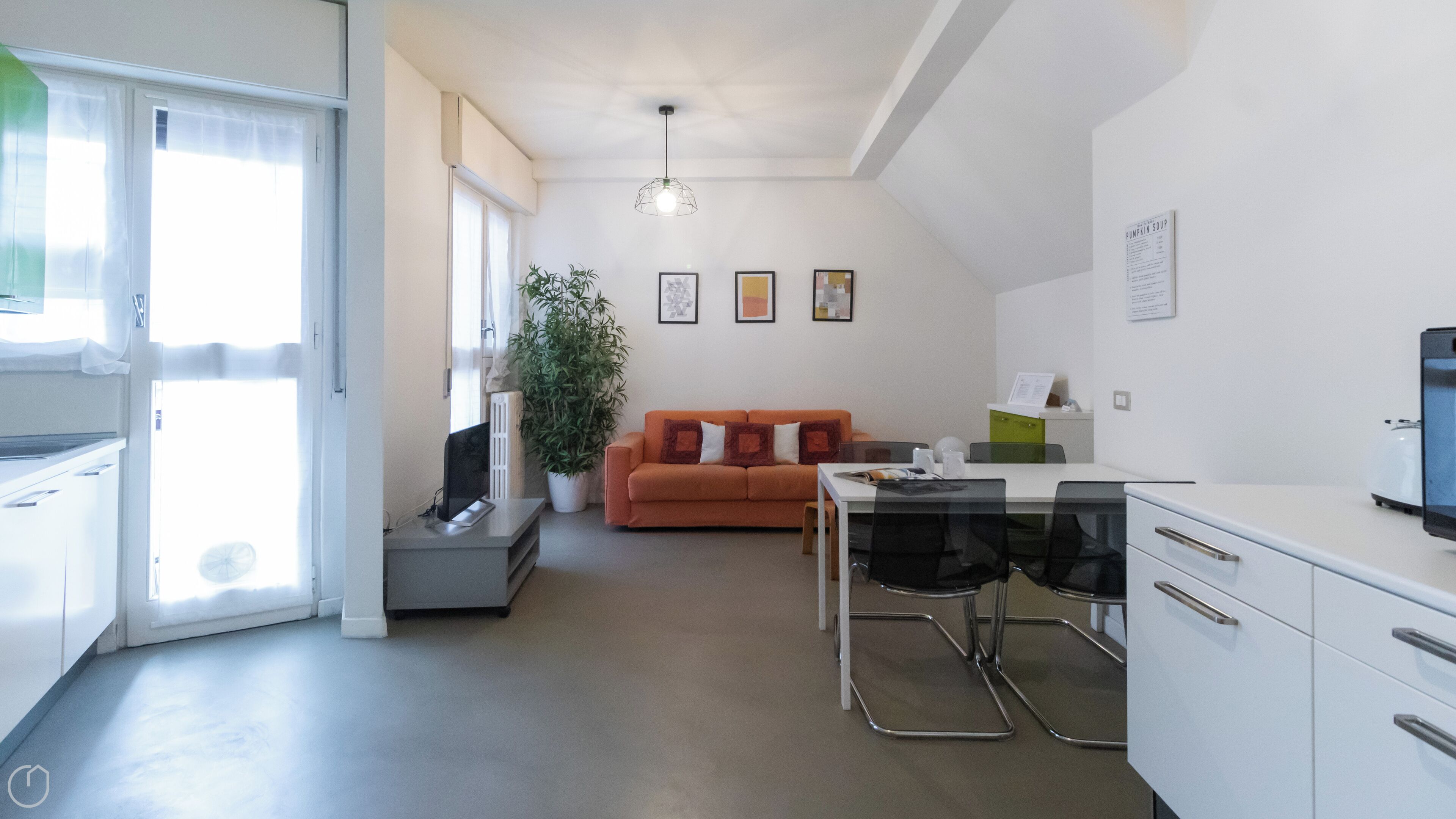 Een moderne woonkamer met een bank, een eettafel met stoelen, een potplant en een keuken met kasten en apparatuur.