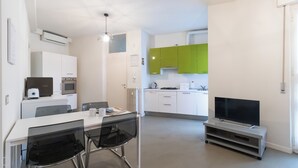 A modern kitchen with white and green cabinets, a dining area with a table and chairs, and a flat-screen TV on a stand. - Italianway Easy - Plinio 64 (Milan)